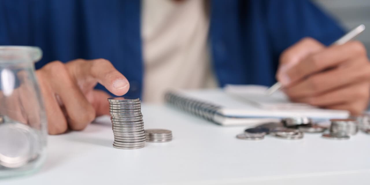 Manos contando monedas sobre un escritorio junto a un cuaderno de registro (imagen de referencia)